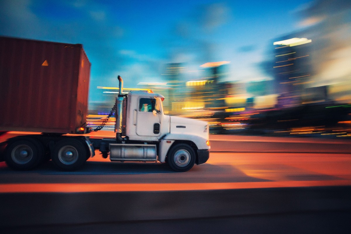 Truck hauling a shipping container through the city at dusk